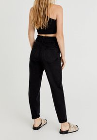 Svarta joggingsbyxor i mjukt material, med elastisk midja, två bakfickor och uppvikta muddar. Bärs med fluffiga sandaler.