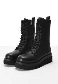 Černé kožené šněrovací boty s designem do poloviny lýtek, robustní gumovou podrážkou a bočním zipem pro snadný přístup. Hladká textura a pevná konstrukce.