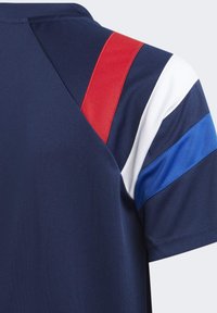 Camiseta deportiva de la marina con acentos en franjas rojas, blancas y azules en los hombros. Fabricada con un tejido suave y transpirable.