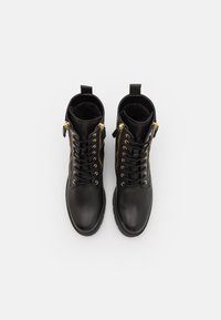 Zwarte leren enkellaarsjes met gouden hardware, voorste veters, zijritsen en een zachte, gestructureerde binnenkant. Vierkante neus en platte zool.