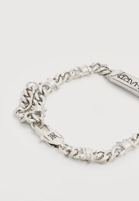 Ασημένιο βραχιόλι με αλυσίδα και ορθογώνια ταμπελίτσα χαραγμένη με τη λέξη "HAPPY" και κούμπωμα με κλιπ αστακού σε λευκό φόντο.