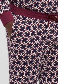 Joggingbroek met een gemarmerd rood en witte geometrische print. Zacht materiaal met een trekkoord in de taille en zijzakken.