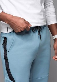 Jasnoniebieskie spodnie dresowe z czarnymi bocznymi zamkami błyskawicznymi, regulowanym paskiem na sznurki i miękkim, teksturowanym materiałem.
