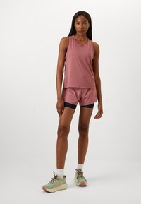 Light pink sleeveless athletic top paired with matching shorts featuring a black waistband, complemented by green and beige sneakers with patterned laces.