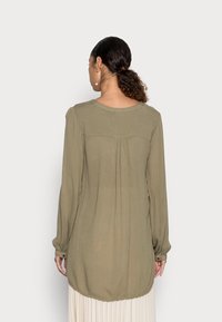 Blouse à manches longues vert olive avec dos plissé, encolure ronde et poignets à boutons, fabriquée en tissu léger et texturé.