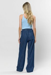 Tricou fără mâneci de culoare albastru deschis, cu dungi, asortat cu pantaloni largi din denim închis la culoare, cu talie elastică și buzunar pe lateral, văzuți din spate.