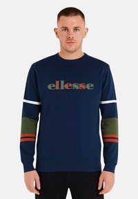 Sweat-shirt bleu marine à encolure ronde, arborant un grand logo "ellesse" aux couleurs douces. Accents rayés verts et oranges sur les manches.