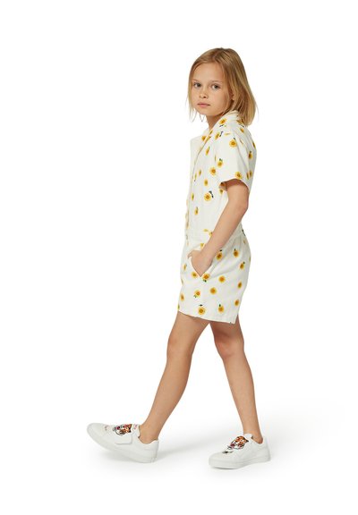 Salopette blanche avec un motif de tournesols jaunes, manches courtes, taille élastique et poches latérales. Portée avec des baskets blanches ornées d'un design de tigre.