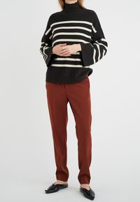 Suéter de cuello alto a rayas en blanco y negro con mangas acampanadas, combinado con pantalones tapered de color óxido y zapatillas negras sin cordones.