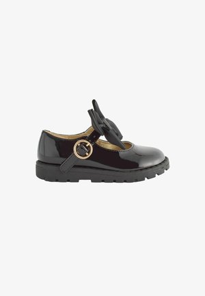 Zapato de charol negro con punta redondeada, correa ajustable con hebilla dorada y un lazo decorativo de tela negra en la parte frontal.