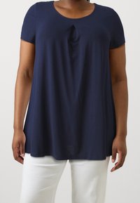 Marinblå topp med kort ärm och rundad halsringning samt en subtil knutdetalj framtill. Tillverkad av mjukt, lätt tyg med en avslappnad passform.