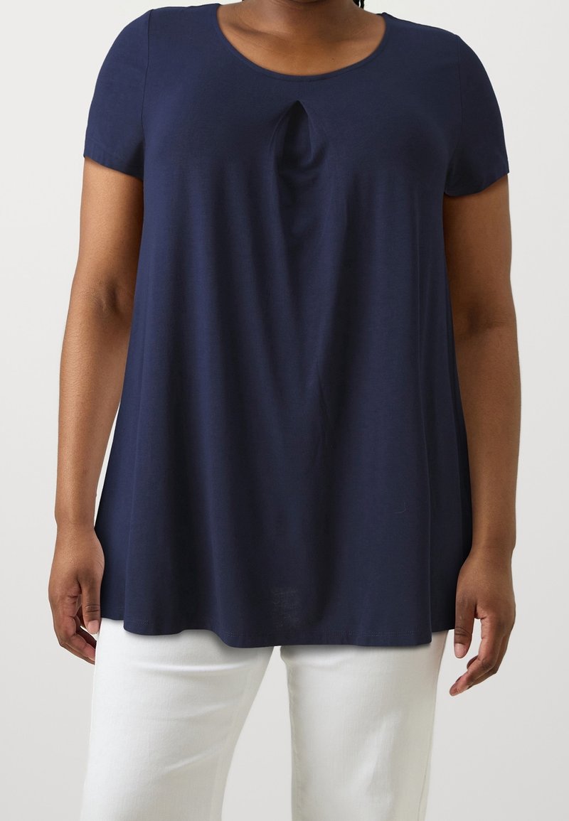 Marinblå topp med kort ärm och rundad halsringning samt en subtil knutdetalj framtill. Tillverkad av mjukt, lätt tyg med en avslappnad passform.