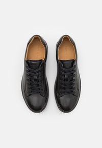 Černé kožené tenisky s hladkým povrchem, zaoblenou špičkou, šněrováním a hnědým vnitřním podšíváním.