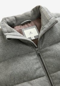 Szara kurtka puchowa z wysokim kołnierzem, zamkiem błyskawicznym i poziomym pikowaniem. Podszewka z gładkiego brązowego materiału; widoczna metka wewnątrz.