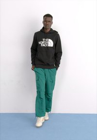 Zwarte hoodie met het logo van "The North Face", groene cargobroek en witte sneakers. Eenvoudig ontwerp, casual fit, textuurstof en grote zakken.