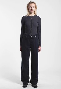 Donkergrijs geribd shirt met lange mouwen en knoopsluiting aan de voorkant, gecombineerd met hoge taille, zwart wijde broek. Textuur van de stof zichtbaar.