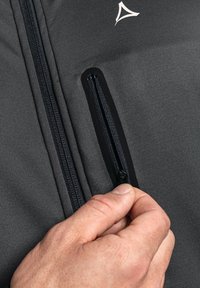 Gray jacket fabric with two zippered pockets. Zippers contrast in dark tones. A small white logo is centered near the neckline.