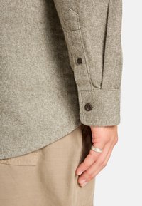 Bruine textuur langslieved shirt met knoopmanchetten, gecombineerd met beige broek. Heeft een subtiel geweven patroon en een afgeronde zoom.