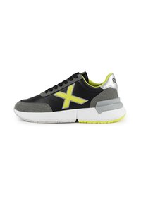 Chaussure de sport noire et grise avec un logo jaune fluo, des accents en daim texturé et une semelle intermédiaire blanche. Lacets et col rembourré inclus.