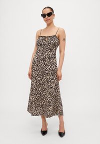 Robe midi à imprimé léopard avec bretelles spaghetti, détail froncé au niveau de la poitrine, jupe fluide et finition en tissu lisse. Portée avec des lunettes de soleil noires.