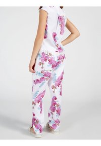 Kwiatowy dwuczęściowy zestaw z białym tłem i różowymi oraz niebieskimi wzorami storczyków. Bluzka ma krótkie rękawy; spodnie mają koronkowe akcenty.