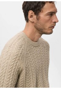 Maglione beige a trecce con scollo rotondo, motivo strutturato e polsini a costine. Materiale morbido mostrato di profilo.
