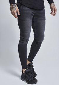 Svarta smala jeans med en blek finish, med femfickorsdesign och kontrasterande sömmar, i kombination med svarta atletiska sneakers.