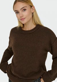 Maglione marrone lavorato a maglia con collo rotondo, spalle scese e polsini a costine. Texture morbida, vestibilità ampia e design minimalista.