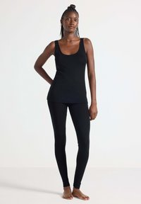 Zwarte tanktop en leggings van zacht, rekbaar materiaal, met een scoop halslijn en een aansluitende pasvorm, gecombineerd met blote voeten.