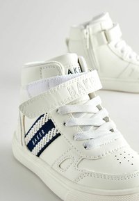 Weiße High-Top-Sneaker aus Leder mit einem Klettverschluss, marineblauen und weißen Streifenakzenten, strukturiertem Profil und durchlöchertem Zehenbereich.