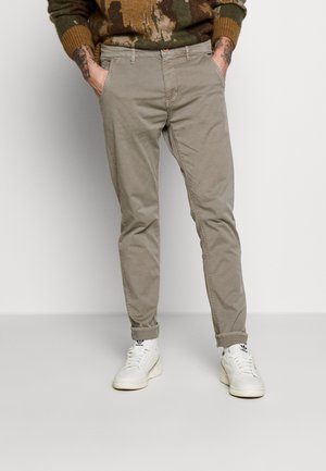 Chinos de algodón beige con un corte ajustado, que cuentan con bolsillos laterales y puños enrollados, combinados con zapatillas blancas. La tela tiene una textura suave.