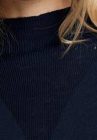 Dunkelblaues, geripptes Strickpullover mit hohem Hals und einem strukturierten Muster mit einem dreieckigen Design auf der Vorderseite.