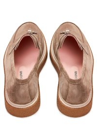 Paire de mocassins en daim marron clair avec pompons, semelles intérieures roses et semelles épaisses en caoutchouc texturé, vue de dessus.