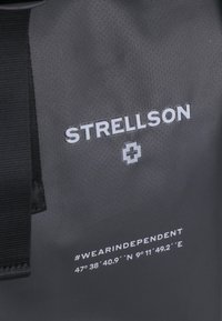Sac étanche noir présentant le logo "STRELLSON" en texte blanc réfléchissant, avec "#WEARINDEPENDENT" et des coordonnées imprimées en dessous.
