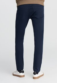 Granatowe dżinsy o slim fit, z dwiema tylnymi kieszeniami i gładką fakturą. Noszone z białymi trampkami z czarnymi akcentami.