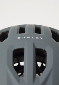 Mattgrauer Oakley Fahrradhelm mit Belüftungsöffnungen, von vorne gegen einen schlichten weißen Hintergrund betrachtet.