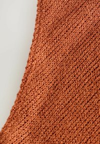 Tissu tricoté couleur rouille avec un motif en relief texturé, présentant un tissage lâche et une apparence douce et flexible.