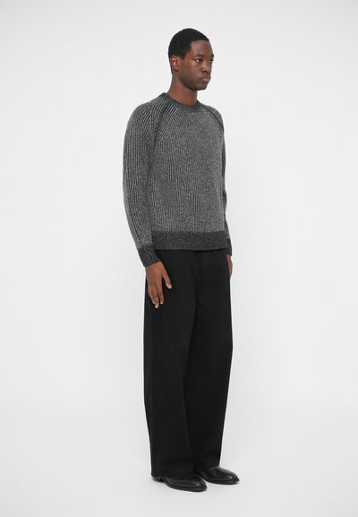 Γκρι υφασμάτινο πουλόβερ με ριγέ μοτίβο, στρογγυλή λαιμόκοψη και μακριά μανίκια, συνδυ�ασμένο με μαύρες φαρδιές παντελόνες και μαύρα παπούτσια.