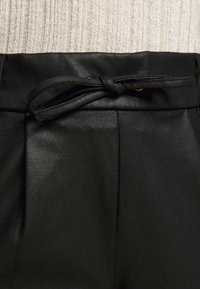 Černé kalhoty s hladkou, texturovanou tkaninou. Vlastnosti zahrnují utažený pas a ostré záhyby pro strukturovaný design.