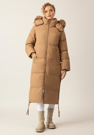 Brauner gepolsterter langer Mantel mit einer mit Pelz gefütterten Kapuze, Frontreißverschluss, Seitentaschen und verstellbaren Bändern am Saum, kombiniert mit beigen Stiefeln.