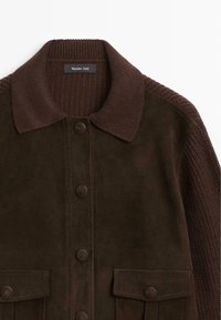 Mørkebrun jakke med strikket krave og ærmer, knaplukning fortil og to lommer med klap fortil.