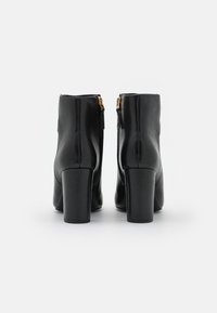 Svarta läderankelstövlar med blockklackar, med en slät yta och detaljer i guld på dragkedjan bak. Strukturerad design, minimalistisk stil.