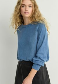 Modrý, měkký svetr s kulatým výstřihem a volnými, nabíranými rukávy. V kombinaci s černou, obepnutou koženou sukní.