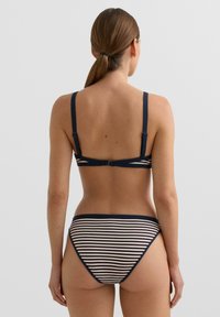 Csíkos bikini állítható tengerészkék pántokkal, testhez simuló bralette felsővel és alacsony derekú alsóval, krém és tengerészkék színösszeállításban. Sima textúrájú.