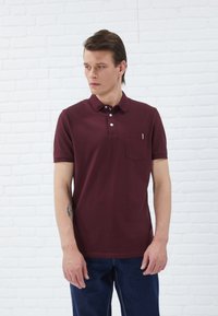 Burgundia polo särk, millel on krae, lühikesed varrukad, ühe rinna-tasku triibuline detail, kombineeritud siniste teksadega.