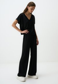 Zwarte oversized V-hals top, gecombineerd met brede zwarte broek. Glad materiaal, ruime pasvorm en witte sneakers maken de look compleet.