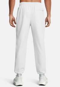 Weiße Sweatpants mit einem elastischen Taillenbund, schmal zulaufenden Bündchen und einer Gesäßtasche. Aus einem glatten Stoff gefertigt. Getragen mit weißen Sportschuhen.