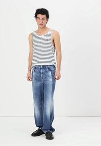 Gestreept wit tanktop met blauwe lijnen, gecombineerd met lichtblauwe denimjeans met vervaagde accenten. Schoenen zijn zwart en chunky.