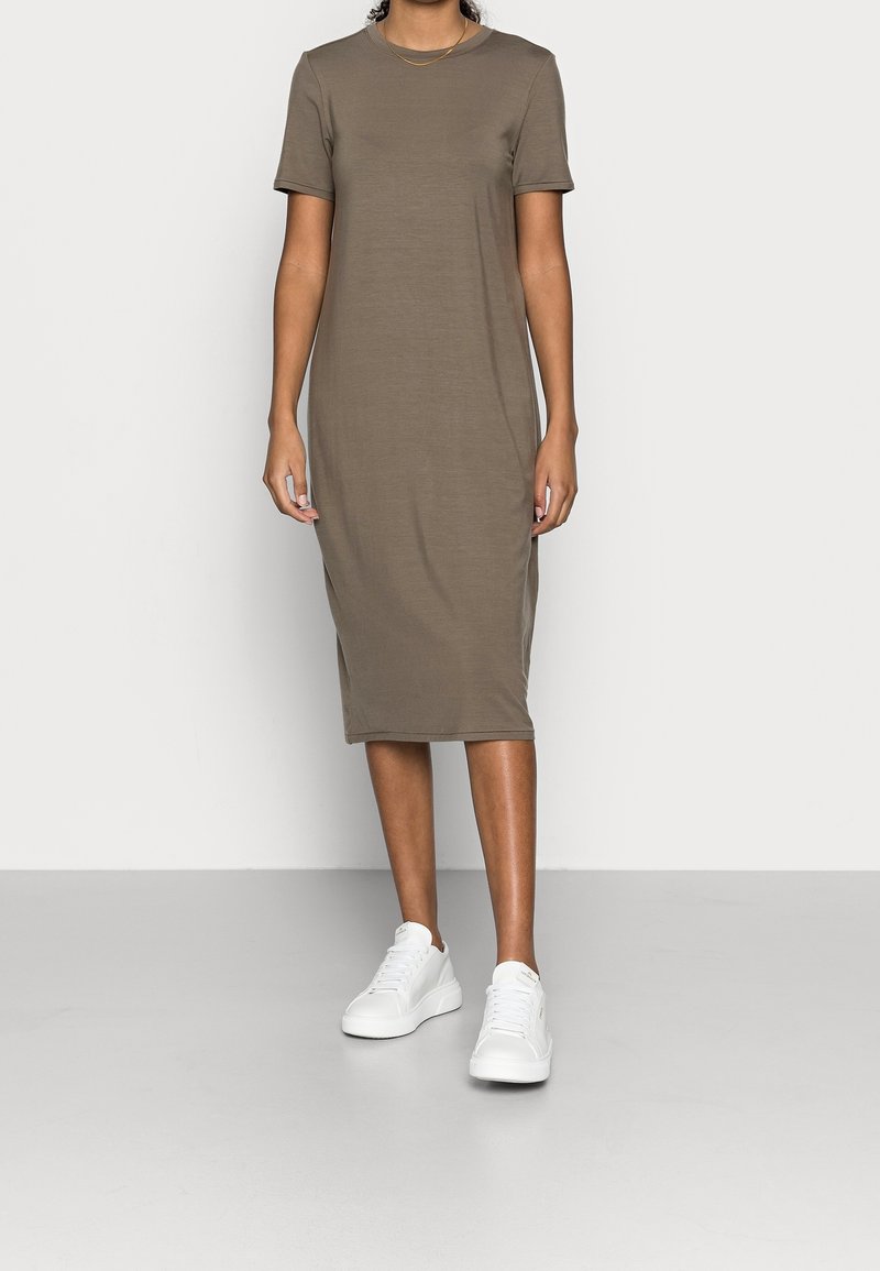 Khaki sukienka z krótkim rękawem, okrągłym dekoltem, sięgająca do połowy łydki, o gładkiej fakturze, zestawiona z białymi trampkami. Minimalistyczny design.