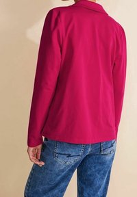 Chemise fuchsia à manches longues avec col, texture lisse et coupe droite, associée à un jean en denim bleu avec des détails de couture subtils.